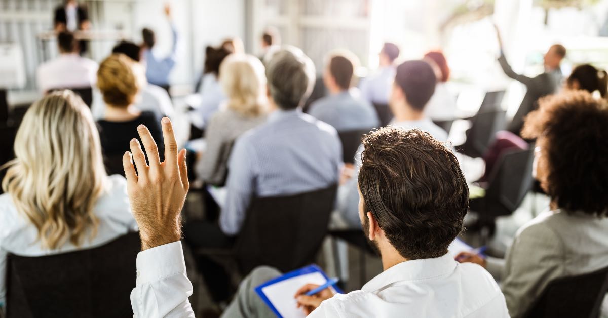 Pessoas levantando a mão em uma palestra sobre aprendizagem corporativa