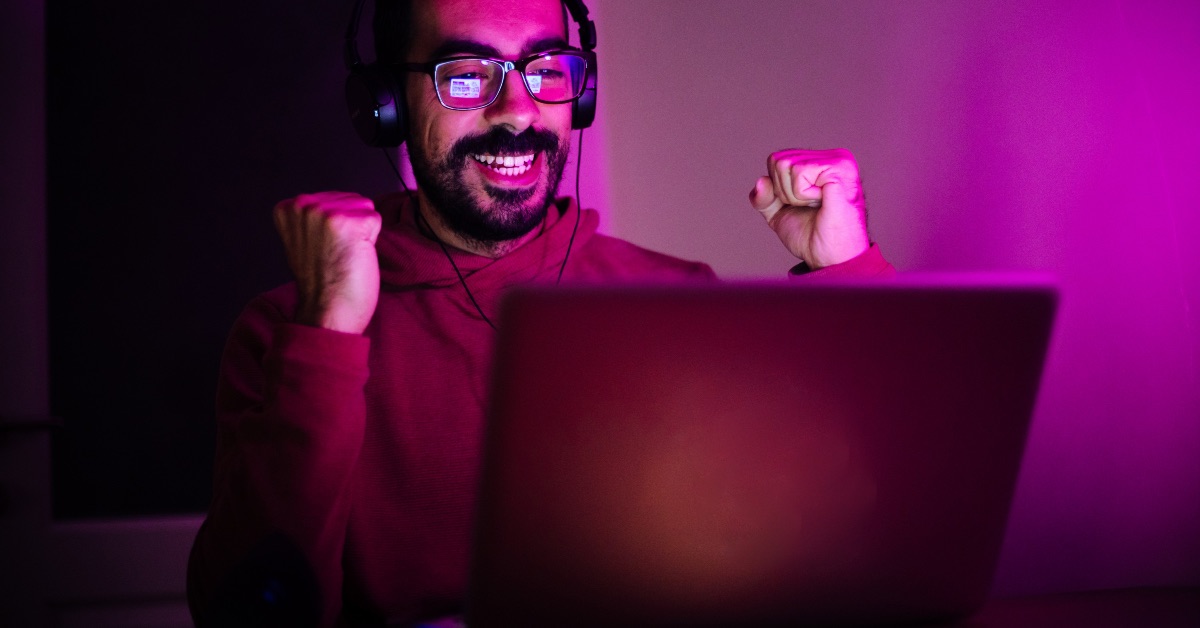 Homem em seu computador, feliz, pesquisando por games e gamificação.